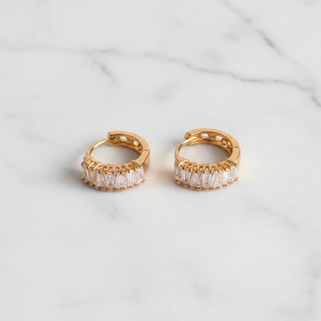 Capri gold plated baguette crystal huggie earrings flat lay on white marble