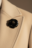 Black enamel rose brooch with gold trim pinned on cream cashmere coat