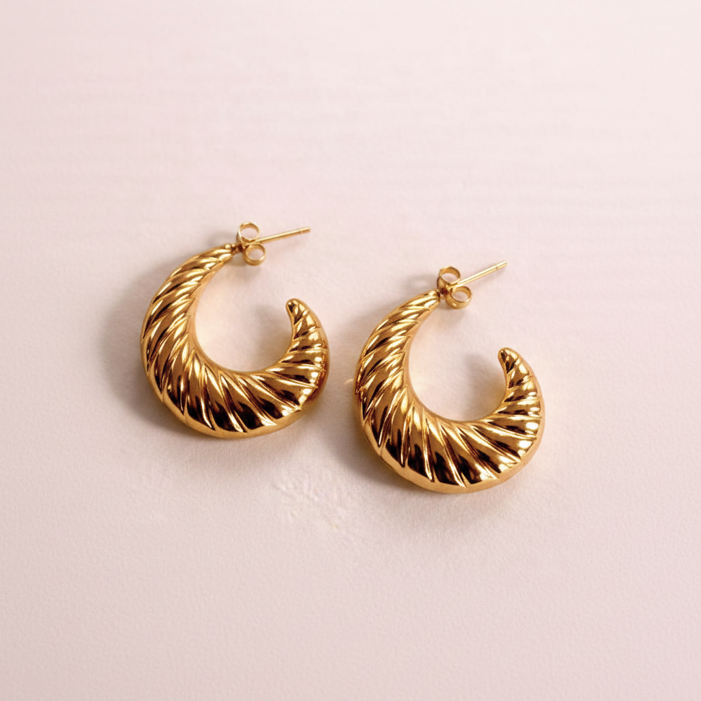Genet gold ribbed shrimp hoop earrings flat lay on blush pink surface
