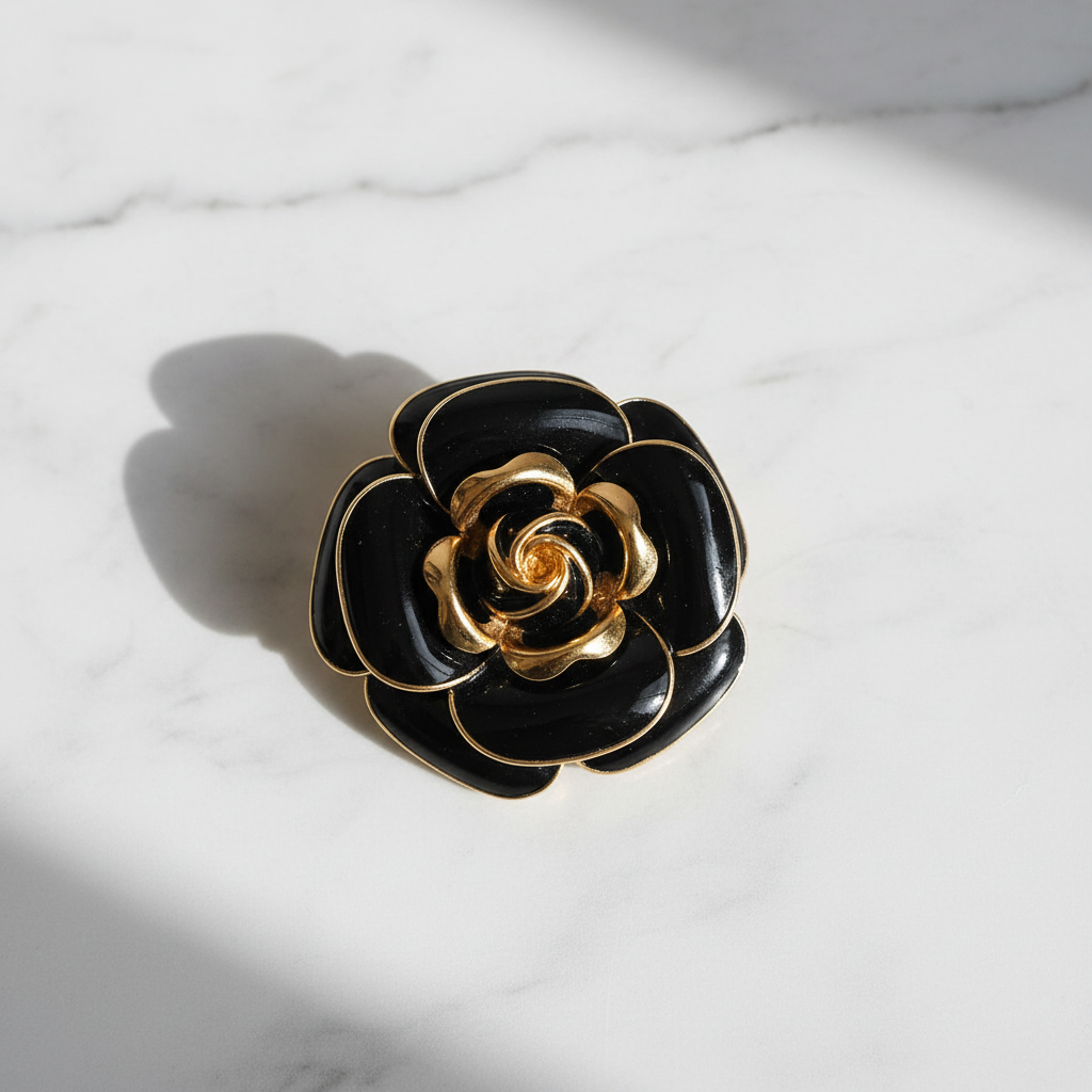 Black enamel rose brooch with gold trim flat lay on white marble