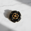 Black enamel rose brooch with gold trim flat lay on white marble